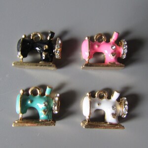 Könnte beinhalten: Vier Miniatur-Nähmaschinen-Anhänger mit goldenen Akzenten. Die Anhänger sind schwarz, rosa, türkis und weiß.