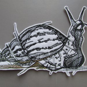 May include: Black and white embroidered snail patch with a detailed shell and antennae. The snail is lying on its side with its shell facing up.