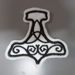 Könnte beinhalten: Ein weißer Filz-Patch mit einem schwarzen gestickten Design eines stilisierten Hammers mit komplizierten Details. Der Hammer ist ein Symbol für Thor, den nordischen Gott des Donners.
