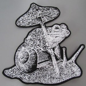 May include: Embroidered patch with a whimsical design of a frog riding a snail, holding a mushroom. The patch is in black and white, with detailed stitching. The patch is approximately 10 cm wide and 7.6 cm tall.