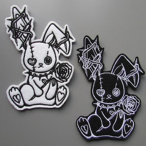 May include: Two embroidered patches featuring a sitting bunny with a gothic aesthetic. One patch is white with black detailing, the other is black with white detailing. Both have thorns, roses, and heart details.