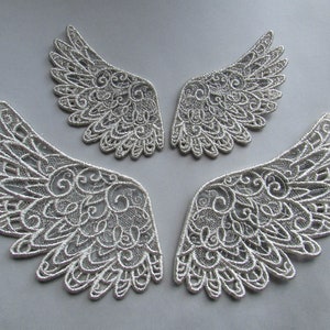May include: Three silver lace angel wings with intricate designs. The wings are delicate and have a soft, feminine feel.