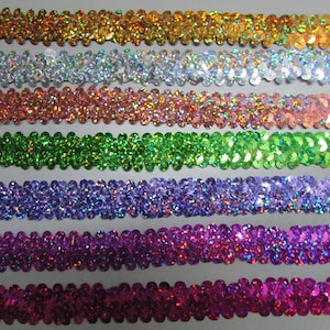 May include: A close-up of seven rows of iridescent sequins in various colors, including gold, silver, pink, green, purple, and magenta. The sequins are arranged in a wavy pattern and are perfect for adding sparkle to crafts and clothing.