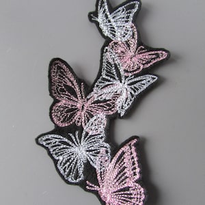 May include: Embroidered patch featuring four butterflies in a cluster. The butterflies are pink and silver with black outlines. The patch is on a black background.