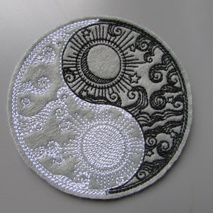 Könnte beinhalten: Ein gesticktes Yin-Yang-Symbol in Schwarz und Weiß mit einem Sonnen- und Monddesign. Sonne und Mond sind von Sternen und Wolken umgeben.