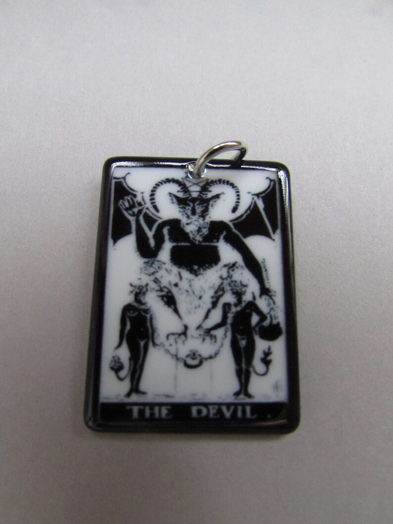 May include: Black and white tarot card pendant with a black border. The card depicts a devil with horns and a goat-like face. The card reads "THE DEVIL".