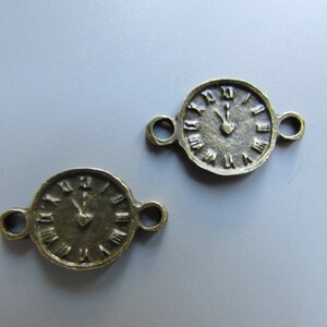 Puede incluir: Dos encantos de cara de reloj de color dorado antiguo con bucles abiertos a cada lado. Las caras de los relojes tienen números romanos y una sola mano apuntando al 12.