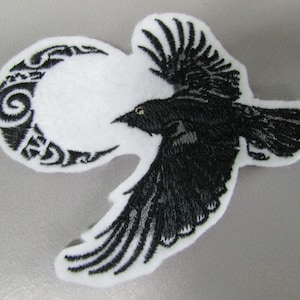 May include: Black embroidered patch of a crow flying with a crescent moon behind it. The moon is decorated with a tribal design.