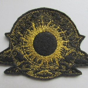 May include: Black felt patch with a gold embroidered design of a sun with rays and a circle of intricate details around it.
