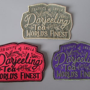 May include: Three embroidered patches with the text "Darjeeling Tea, World's Finest". The patches are in shades of green, red, and purple, with the text in a contrasting colour. The patches also say "Product of India".
