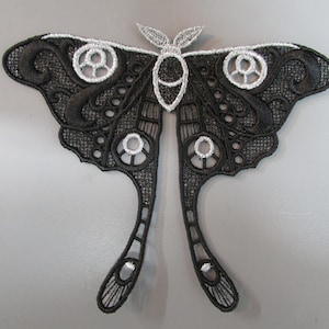 Può includere: Applicazione a forma di falena ricamata in nero e argento. La falena presenta dettagli intricati con ali traforate e un delicato design di antenne. Le ali hanno accenti circolari e caratteristiche allungate a forma di coda. Questa applicazione decorativa è adatta per abbigliamento o progetti artigianali.