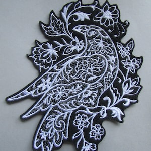 Peut inclure: Patch thermocollant brodé noir et blanc représentant un oiseau stylisé avec des détails floraux complexes.