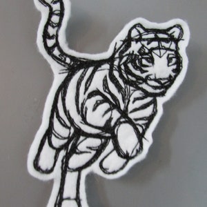 May include: Black and white embroidered patch of a tiger running. The tiger is outlined in black thread on a white fabric background.