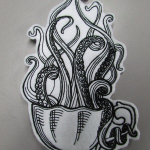 May include: Black and white embroidered patch depicting an octopus emerging from a teacup. The octopus's tentacles are curled and swirling around the cup.