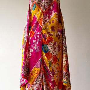 May include: A colourful floral-print dress with a V-neck and spaghetti straps. The dress has a patchwork design in pink, yellow, and orange. The dress is displayed on a mannequin.