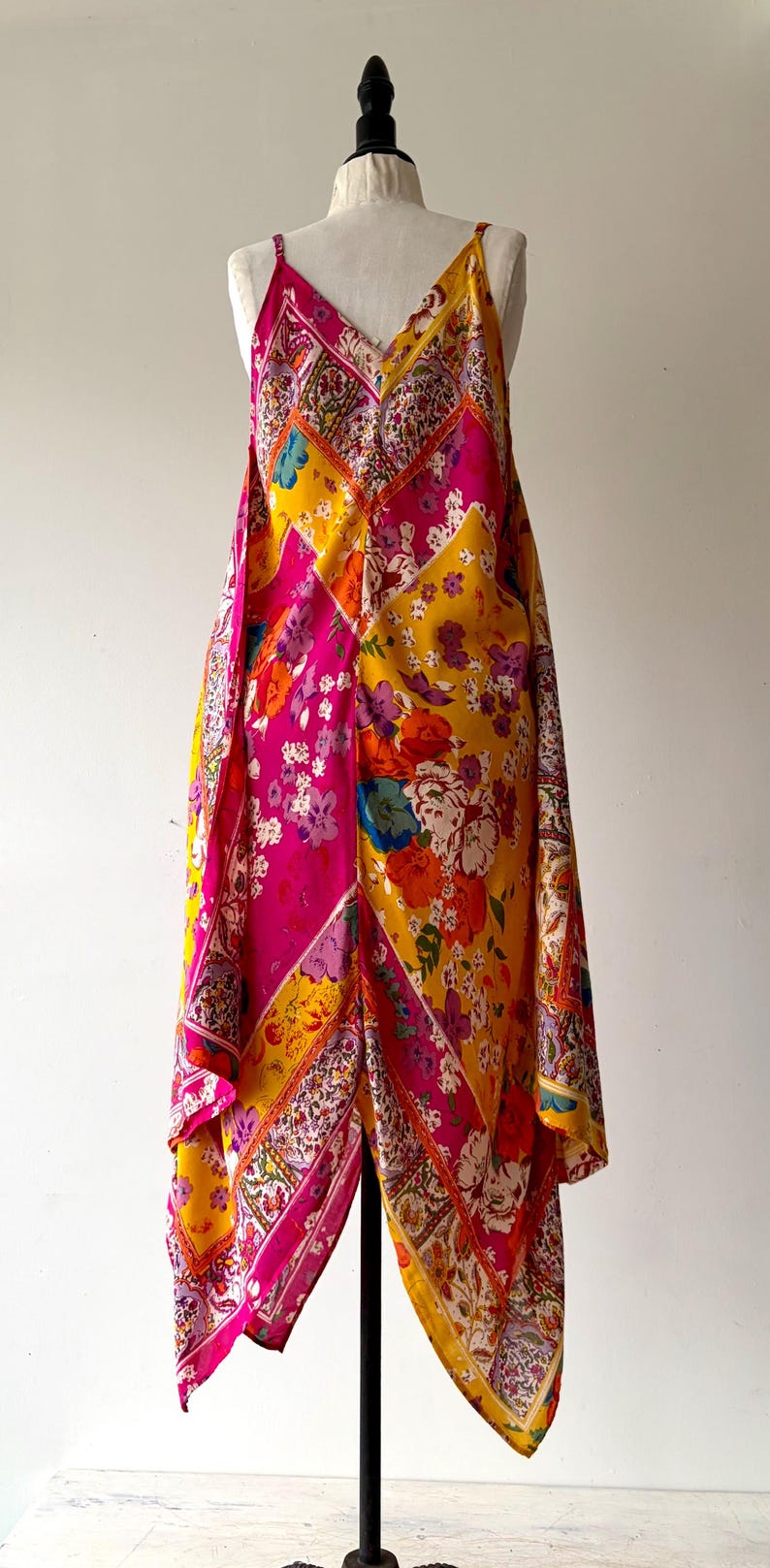 May include: A colourful floral-print dress with a V-neck and spaghetti straps. The dress has a patchwork design in pink, yellow, and orange. The dress is displayed on a mannequin.