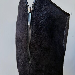 May include: Close-up of a black suede boot with a silver zipper. The zipper runs vertically along the side of the boot. The brand name "DONALD PLINER" is visible on the zipper pull. The boot has a sleek, modern design.