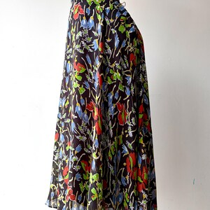Peut inclure: Longue jupe fluide avec un fond sombre et un motif floral vibrant. Le motif pr&eacute;sente des fleurs rouges, bleues et vertes avec des accents blancs. La jupe est pr&eacute;sent&eacute;e sur un mannequin.