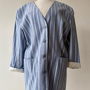 May include: A blue and white striped blazer featuring a V-neckline, four front buttons, and two front pockets. The long sleeves have white cuffs that are folded upward. The garment is displayed on a mannequin against a plain white background.