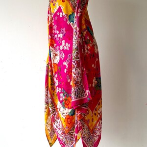 May include: A colourful patterned dress in pink, yellow, and red, displayed on a black mannequin. The dress features a floral design with a mix of colours and patterns. The dress is sleeveless and has a flowing, asymmetrical hemline.