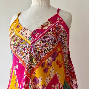 May include: A patterned dress with a V-neck and spaghetti straps. The dress features a patchwork design with vibrant pink, yellow, and floral patterns. The dress is displayed on a mannequin.