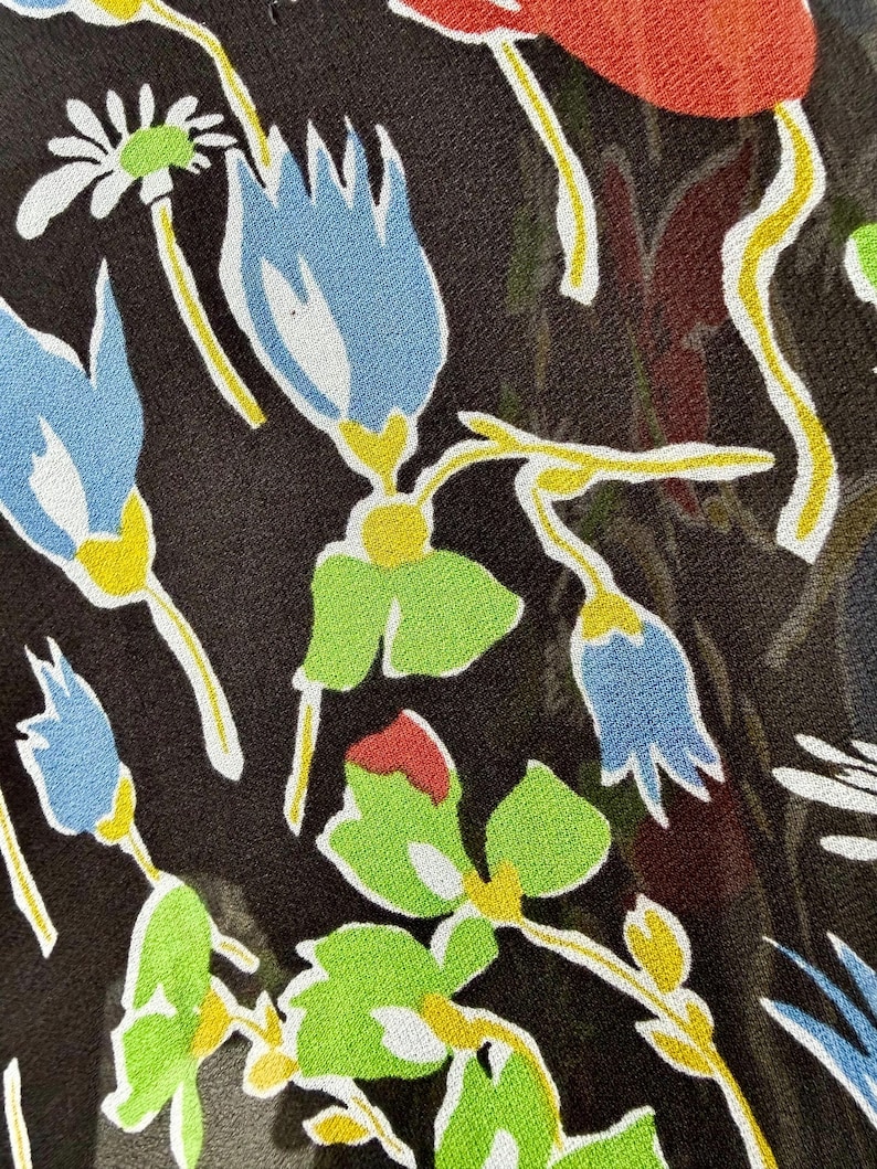 Peut inclure: Gros plan sur un tissu &agrave; motifs floraux. Le motif pr&eacute;sente des fleurs bleues, rouges et blanches avec des feuilles vertes et des tiges jaunes sur un fond marron fonc&eacute;. Les fleurs sont stylis&eacute;es.