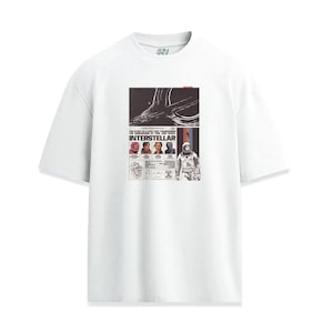 May include: White t-shirt featuring a graphic from the movie "Interstellar." The design includes the film's title, images of the cast, and space-themed illustrations. The shirt has a crew neck and short sleeves.