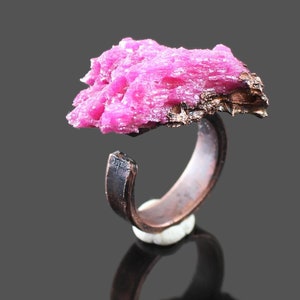 May include: A pink crystal ring with a copper band. The crystal is a cluster of small, pointed crystals.