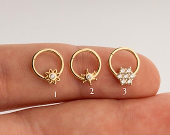 May include: Three gold hoop earrings with different gemstone accents. The first earring has a flower design, the second has a star design, and the third has a cluster of small gemstones.