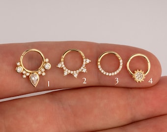 May include: Four gold-toned hoop earrings with different crystal embellishments. The first earring has a teardrop-shaped crystal with smaller crystals surrounding it. The second earring has a row of crystals around the hoop. The third earring has a row of crystals around the hoop. The fourth earring has a sun-shaped crystal with smaller crystals surrounding it.