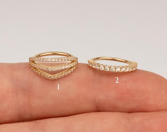 May include: Two gold septum rings with clear cubic zirconia stones. The first ring has three rows of stones in a chevron shape. The second ring has a single row of stones.