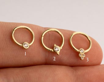 May include: Three gold hoop earrings with different diamond accents. The first earring has a single round diamond, the second earring has a triangular diamond, and the third earring has a cluster of small diamonds.