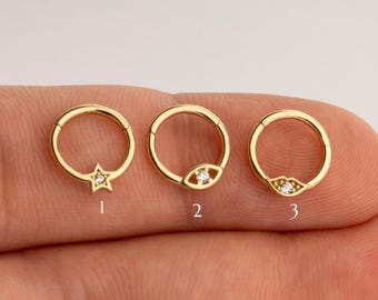 May include: Three gold hoop earrings with different charms. The first earring has a star charm, the second earring has an eye charm, and the third earring has a lip charm.