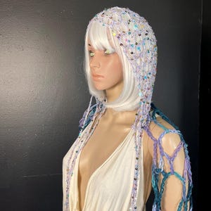 May include: A white, sequined hood and shoulder wrap. The hood is made of a delicate, open weave, adorned with iridescent sequins. The shoulder wrap features a blue and purple open weave design, creating a unique, ethereal look.