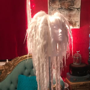 Puede incluir: Peluca de rastas blancas en una cabeza de maniqu&iacute;, la peluca es larga y fluida, el maniqu&iacute; est&aacute; en un soporte con una base de tr&iacute;pode.