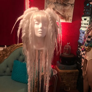 Puede incluir: Una peluca de rastas sint&eacute;ticas blancas con flequillo en una cabeza de maniqu&iacute;. La peluca se muestra en un tr&iacute;pode.