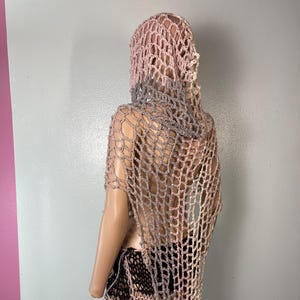 May include: A handmade crochet outfit in shades of pink, gray, and black. The outfit includes a hooded shawl and a skirt. The open weave design creates a net-like appearance. The mannequin is positioned against a gray and pink wall.