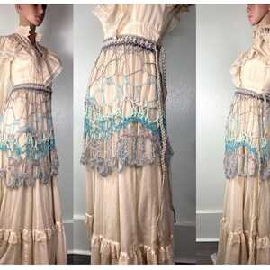 May include: A long, white, crocheted skirt with a blue and white pattern. The skirt is layered and has a ruffled hem. It is worn over a white dress with a lace bodice.