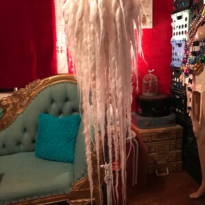 Puede incluir: Peluca de rastas blancas en un tr&iacute;pode. La peluca es larga y gruesa, de color blanco.
