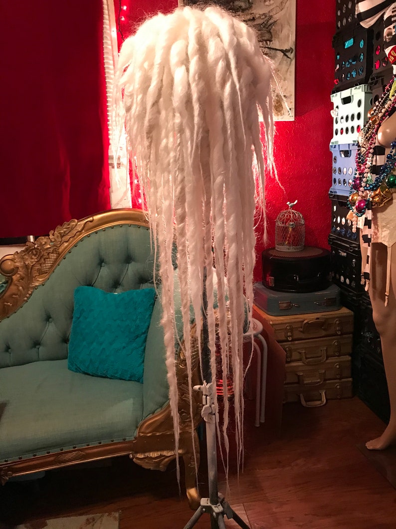 Puede incluir: Peluca de rastas blancas en un tr&iacute;pode. La peluca es larga y gruesa, de color blanco.