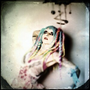 Puede incluir: Una mujer con el pelo de colores y tatuajes lleva un vestido rosa y blanco. Mira hacia arriba a un m&oacute;vil que cuelga del techo.