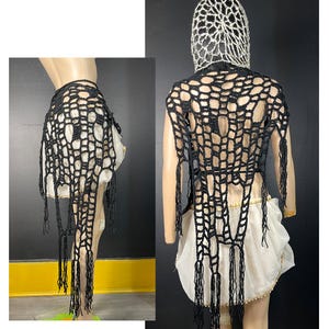 Peut inclure: Châle en crochet noir avec des franges. Le châle est de forme rectangulaire et présenté sur un mannequin portant une jupe blanche et une coiffe en crochet blanche.