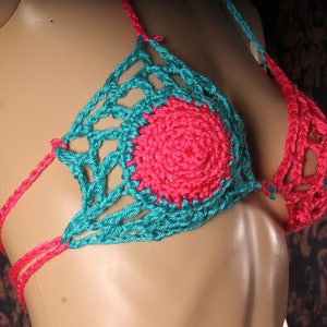 May include: A teal and pink crocheted bikini top with a circular design in the center.