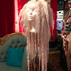 Puede incluir: Una peluca blanca con rastas largas y gruesas en una cabeza de maniqu&iacute;. La peluca est&aacute; peinada con un flequillo recto y las rastas cuelgan rectas hacia abajo.