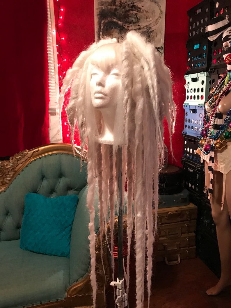 Puede incluir: Una peluca blanca con rastas largas y gruesas en una cabeza de maniqu&iacute;. La peluca est&aacute; peinada con un flequillo recto y las rastas cuelgan rectas hacia abajo.