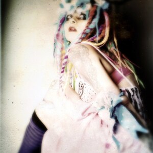 Puede incluir: Una mujer con el pelo de colores y un vestido rosa. Lleva una diadema blanca con un patr&oacute;n azul y blanco. El fondo est&aacute; desenfocado y fuera de foco.