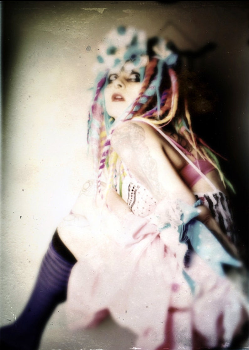 Puede incluir: Una mujer con el pelo de colores y un vestido rosa. Lleva una diadema blanca con un patr&oacute;n azul y blanco. El fondo est&aacute; desenfocado y fuera de foco.