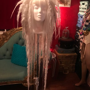 Puede incluir: Peluca blanca de rastas en una cabeza de maniqu&iacute;. La peluca es larga y tiene flequillo. El maniqu&iacute; est&aacute; en un tr&iacute;pode.