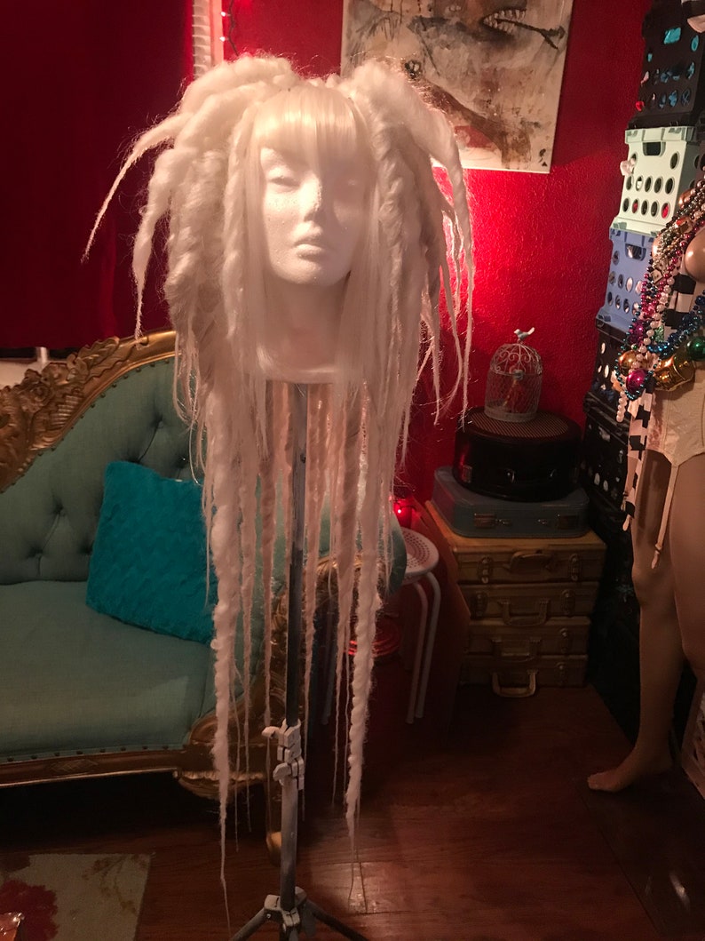 Puede incluir: Peluca blanca de rastas en una cabeza de maniqu&iacute;. La peluca es larga y tiene flequillo. El maniqu&iacute; est&aacute; en un tr&iacute;pode.