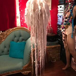 Puede incluir: Peluca de rastas blancas en un tr&iacute;pode. La peluca es larga y fluida, con un fondo blanco.
